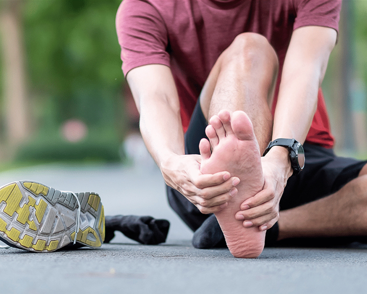 Runner touching the sole of his foot with his hands due to plantar fasciitis pain