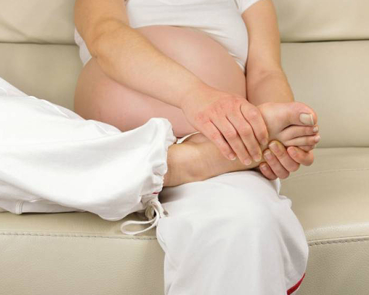 Mujer embarazado tocando la planta de su pie derecho