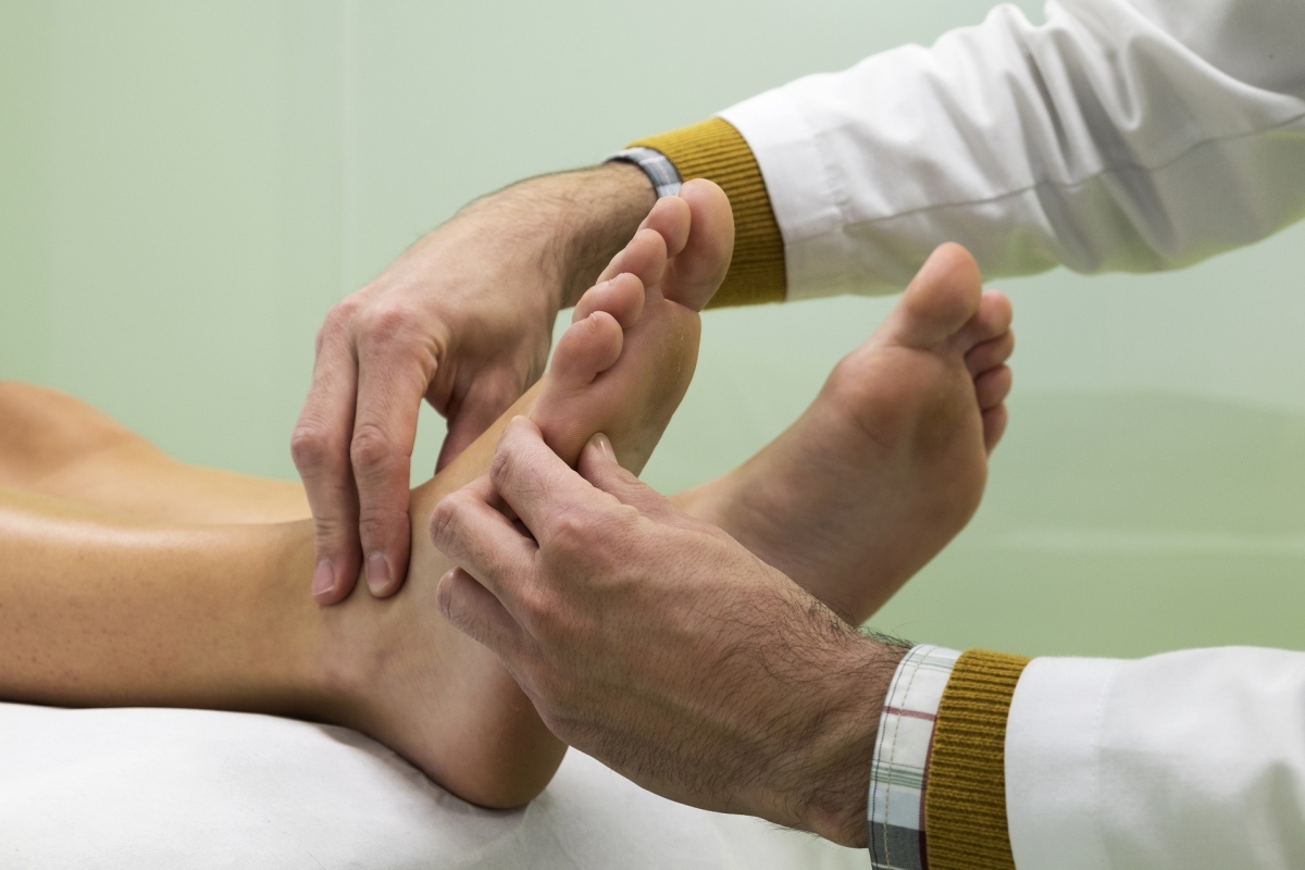 Manos de médico con bata blanca examinando un pie