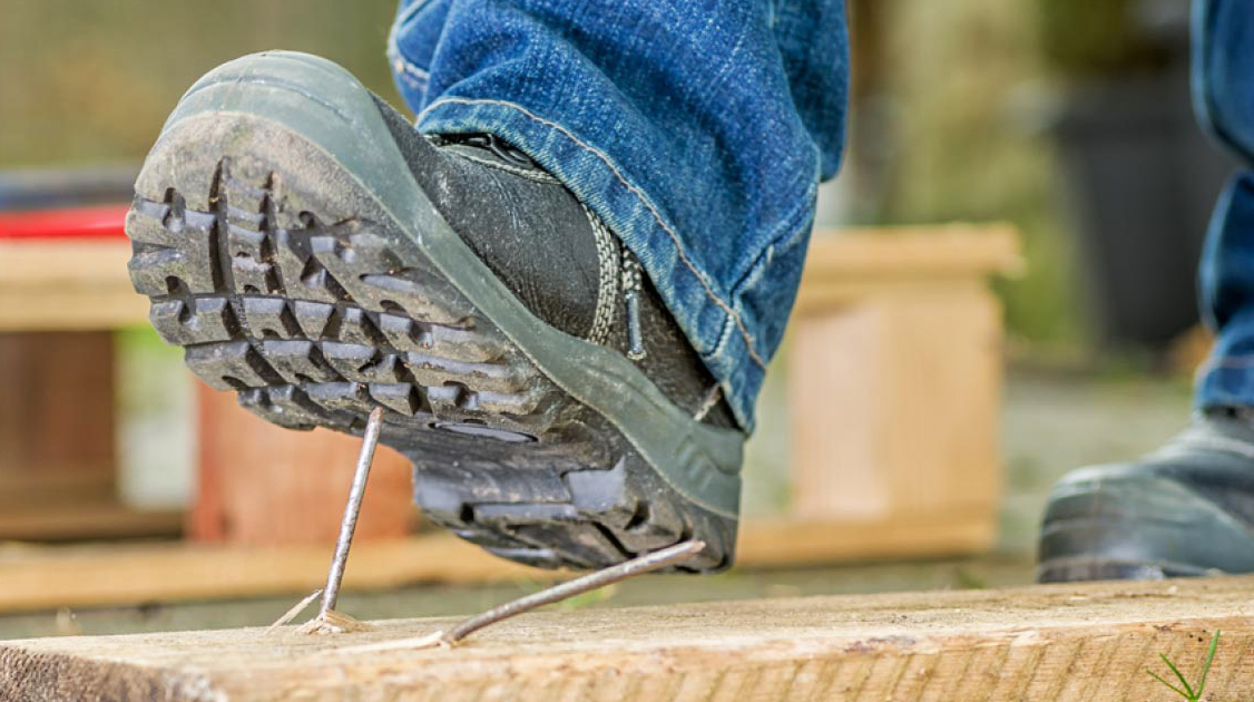 Bota de seguridad sobre un clavo puesto en una tabla de madera