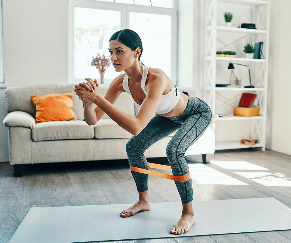 Chica practicando ejercicio en casa con una goma en las piernas